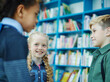 © Comeback Images - Group of three school kids, girl and two boys, standing together and talking friendly near bookshelves in school library