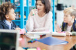 © Comeback Images - Female teacher and two diverse elementary students talking over task sitting at desk in classroom