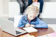 © Comeback Images - Diligent little girl doing homework in notepad sitting at desk in school classroom with open laptop in front of her