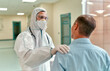 © Valerii Apetroaiei - A young male doctor in a protective suit, glasses, a respirator and medical gloves congratulates the patient on his recovery during the coronavirus or Covid-19 pandemic.