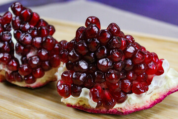 Two pieces of pomegranate with red seeds on a wooden tray. Pomegranate seeds. One piece in front and the other piece of ripe pomegranate fruit behind.