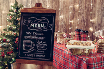 Wall Mural - Christmas pastry shop . Woman seller, waitress selling gingerbread, marshmallows, cookies, sweets and hot chocolate in a small cozy cafe. Homemade bakery menu in the foreground