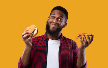 Wall Mural - Happy Black Guy Holding Burger And Pizza On Yellow Background