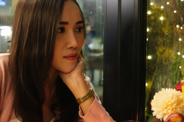 Attractive woman looking out of window on dinner time with beautiful light decoration at night