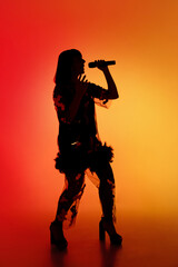 Wall Mural - Talented. Silhouette of young female singer isolated on orange gradient studio background in neon light. Beautiful shadow in action, performing. Concept of human emotions, expression, ad, music, art.