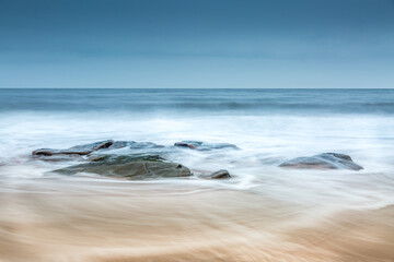 A group of rocks on the beach as the wave backwash returns to the sea over the sand on a cloudy day (2)