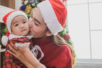 Wall Mural - merry christmas and happy holidays. mother held her daughter near the christmas tree and decorate the christmas tree indoors. portrait loving family close up. mom kisses the child.