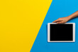 Kid hand holding digital tablet computer on yellow and light blue background