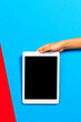 Kid hand with tablet computer on red and light blue background