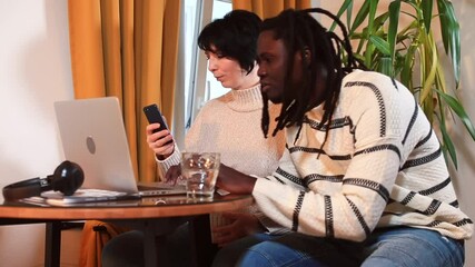 Poster - Afro man and woman sitting at the table make decisions in dialogue. She uses a phone, he uses a laptop. Communication of employees in a team.