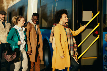 Group of happy people entering a bus at the station.