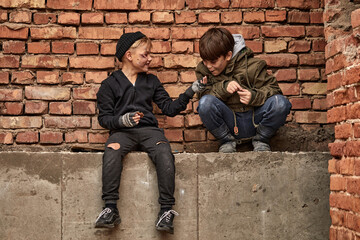 two friendly street boys sharing piece of bread, eating together, beggars in dirty clothes suffering from hunger and poverty