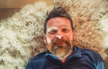 Wall Mural - portrait of happy relaxed man laying on sheepskin rug