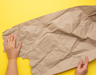 two hand holds piece of crumpled brown paper on a yellow background