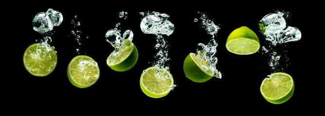 Bunch of lime fruits halves sinking with bubbles into water isolated against black background. Citrus theme, panorama