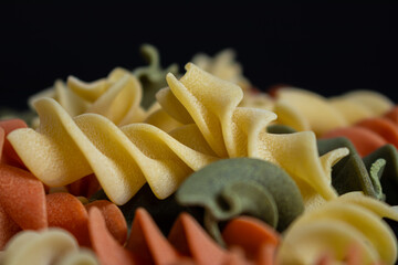 Dry and raw tricolor Italian pasta on black surface. Space to write.