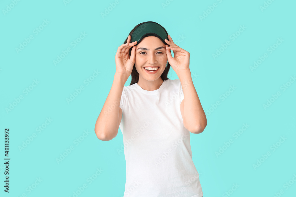 Young woman with sleep mask on color background