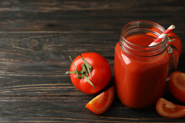 Jar with tomato juice and straw and tomatoes on wooden background