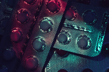 Poster - Pills or drugs in a package under neon light on a dark background pattern for design..
