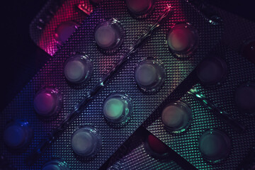 Poster - Pills or drugs in a package under neon light on a dark background pattern for design..