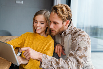 Wall Mural - Masculine focused military man using tablet computer with his smiling daughter