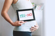 © nataliaderiabina - Pregnant woman holds whiteboard with text message - YES or NO.