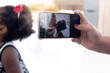 © chomplearn_2001 - Woman's hand taking a picture of mother and daughter with  smartphone, image of African mother and child girl are showing love by kissing