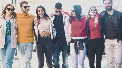 Wall Mural - Joyful Multi-Ethnic group of people smiling while they’re walking and hugging together hands on shoulders in the city center. Friendship and togetherness young people lifestyle concept.