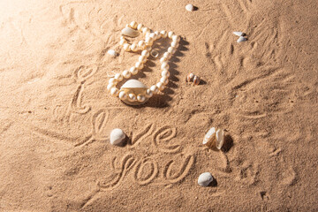 Shells and pearl necklace on the beach sand with romantic phrases written in the sand, selective focus.