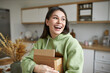 Shipment, delivery, moving and online shopping concept. Happy overjoyed young brunette woman posing indoors with small cardboard parcel in her hands with new books, clothing or food products