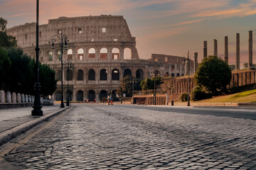 Via dei Fori Imperiali street in the historic center of Rome, Italy, completely deserted, with the Colosseum in the background wrapped in the colors of dawn