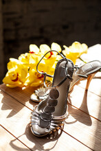 Bride's Shoes And A Branch Of Yellow Orchids On A Wooden Background Lit By A Bright Sun