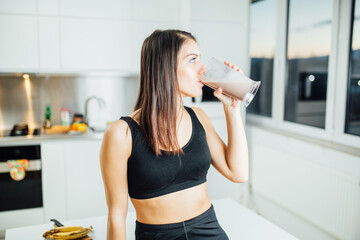 Woman in sportswear drinking sweet banana chocolate protein powder milkshake smoothie.Drinking protein after at home workout.Whey, banana and low fat milk sports nutrition diet.Healthy lifestyle