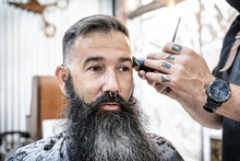 Crop Anonymous Barber With Electric Trimmer And Comb Cutting Hair Of Middle Aged Hipster Male Customer With Long Beard And Mustache In Modern Barbershop
