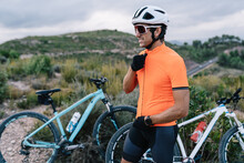 Side View Of Handsome Male Bicyclist Standing In Mountainous Area Near Modern Bikes While Preparing For Ride And Looking Away