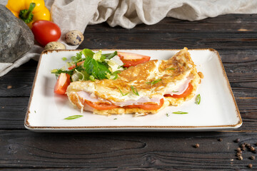 Wall Mural - Omelet with ham, bacon, cheese and tomatoes. Classic hot dish of eggs, milk, meat, cheese, vegetables and salad in a ceramic plate on a wooden kitchen table.