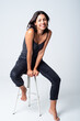 © Galdric Penarroja/ADDICTIVE STOCK - Full length young slim brunette in casual outfit sitting on stool against white background and looking at camera with happy smile