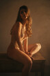 © Gustavo Pozo/ADDICTIVE STOCK - Side view of tranquil female in bodysuit sitting on wooden table and embracing knees while enjoying sunlight looking at camera