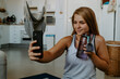 © Jake Jakab/ADDICTIVE STOCK - Smiling young female in sportswear holding water bottle and taking selfie on modern mobile phone during home workout