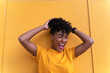 © Jake Jakab/ADDICTIVE STOCK - Happy young African American female with curly hair wearing bright yellow shirt and jeans standing against yellow wall and looking away