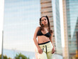 © Jose Carlos Cerdeno/ADDICTIVE STOCK - Young self assured slim ethnic sportswoman in bra and pants standing looking at camera in city park with hands in pockets against modern skyscrapers
