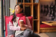 © Luis Gomez/ADDICTIVE STOCK - Thoughtful adult Asian female in trendy warm outfit sitting on chair with cup of takeaway coffee and looking at window while resting in cozy cafeteria