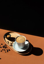 From Above Of Ceramic Cup Of Aromatic Coffee With Milk On Wooden Plate Near Bowl With Cane Sugar On Table With Shade In Sunlight On Black Background