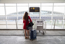 Back View Of Traveling Female In Airport Collecting A Baggage Trolley And Waiting For Flight