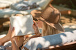 © Philippe Degroote/ADDICTIVE STOCK - Back view young beautiful female traveler in hat reading book while lounging in yard of hotel in sunlight