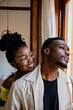 © Rafa Cortes/ADDICTIVE STOCK - Cheerful young African American female in transparent eyeglasses with bunch looking at thoughtful man standing near window