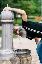 Content Old Male Hipster In Trendy Clothes Drinking Water From Fountain In City While Looking At Camera
