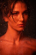 © Sebastian Candiolli/ADDICTIVE STOCK - Attractive young sensual female with bare shoulders and perfect makeup standing behind transparent glass with water drops in red light
