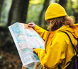 © Albert Morcillo/ADDICTIVE STOCK - Side view of female explorer in yellow raincoat and with backpack standing in woods and searching for route on paper map