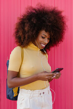 Black Woman With Afro Hair Listening To Music On Mobile In Front Of A Pink Wall